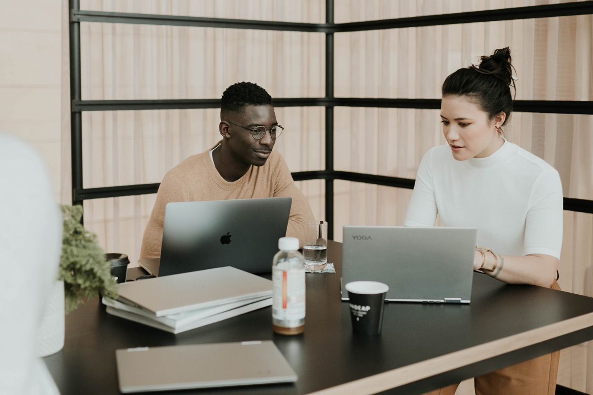Two people working at a table on their laptops